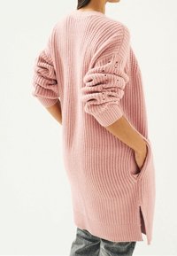 Cárdigan de punto rosa con mangas largas, textura acanalada, bolsillos laterales y aberturas en el dobladillo, con un ajuste relajado.