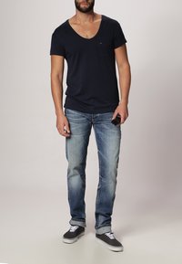 Granatowa koszulka z dekoltem w serek, niebieskie dżinsy i czarne trampki. Koszulka ma kieszonkę; dżinsy charakteryzują się wyblakłym wykończeniem i lekkimi przetarciami.