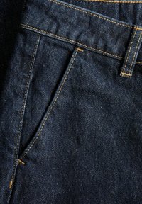 Dark blue denim fabric with yellow stitching showing a close-up of a front pocket and belt loop on jeans.
