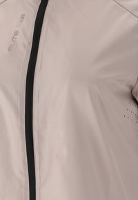 Light beige jacket with a smooth texture, featuring a black zipper and perforated details on the side. Branding "ELITE LAB" in silver.