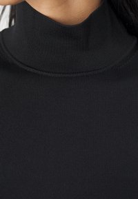 Černý žebrovaný rolák s vysokým límcem. Látka působí měkce a pružně, s přiléhavým střihem a minimálním zdobením ve formě švů.