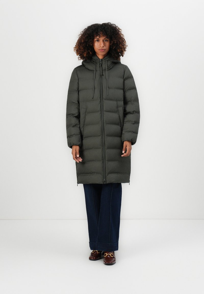 Cappotto puffer verde scuro con cappuccio, dotato di zipper frontale, polsini a coste e cordini elastici, abbinato a jeans larghi scuri.