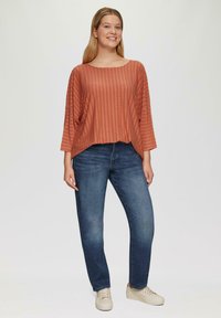 Roodgestreepte, losvallende top met een wijde halslijn en 3/4 mouwen, gecombineerd met blauwe rechte jeans en lichte sneakers.