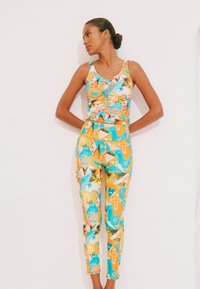 Costum din două piese format dintr-un top mulat fără mâneci și colanți. Materialul prezintă un model vibrant, multicolor, cu motive florale și geometrice.