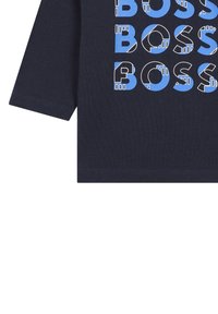 T-shirt en coton bleu marine à manches longues avec un motif géométrique comportant le texte "BOSS" répété en bleu et blanc. Texture douce, col rond.