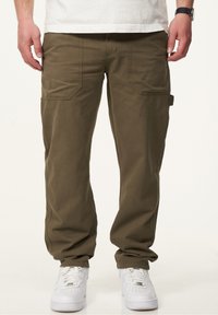 Olivegrüne Cargo-Hosen aus robustem Baumwollmaterial mit mehreren Taschen und einem lässigen Schnitt, kombiniert mit weißen Sneakers.