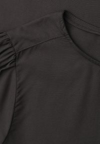 Gros plan de la zone d'épaule d'un vêtement noir avec une manche bouffante plissée et des détails de couture au col rond.