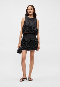 Conjunto de top cropped e saia mini em textura floral preta, apresentando flores em tecido em camadas, combinado com acessórios pretos e sandálias de salto.