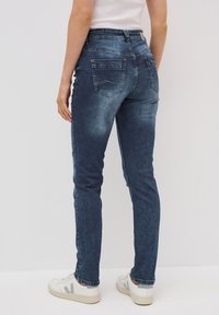Donkerblauwe denim jeans met een slim fit, voorzien van achterzakken en een hoge taille. Gemaakt om te dragen met witte sneakers, met een taps toelopend ontwerp van de pijpen.