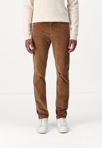 Pantalons en velours côtelé marron avec une coupe droite, présentant des côtes verticales, des poches avant, et assortis à des baskets blanches.