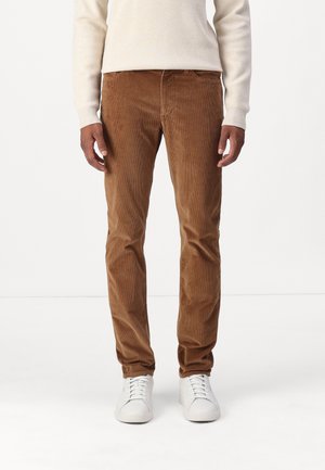 Pantalons en velours côtelé marron avec une coupe droite, présentant des côtes verticales, des poches avant, et assortis à des baskets blanches.
