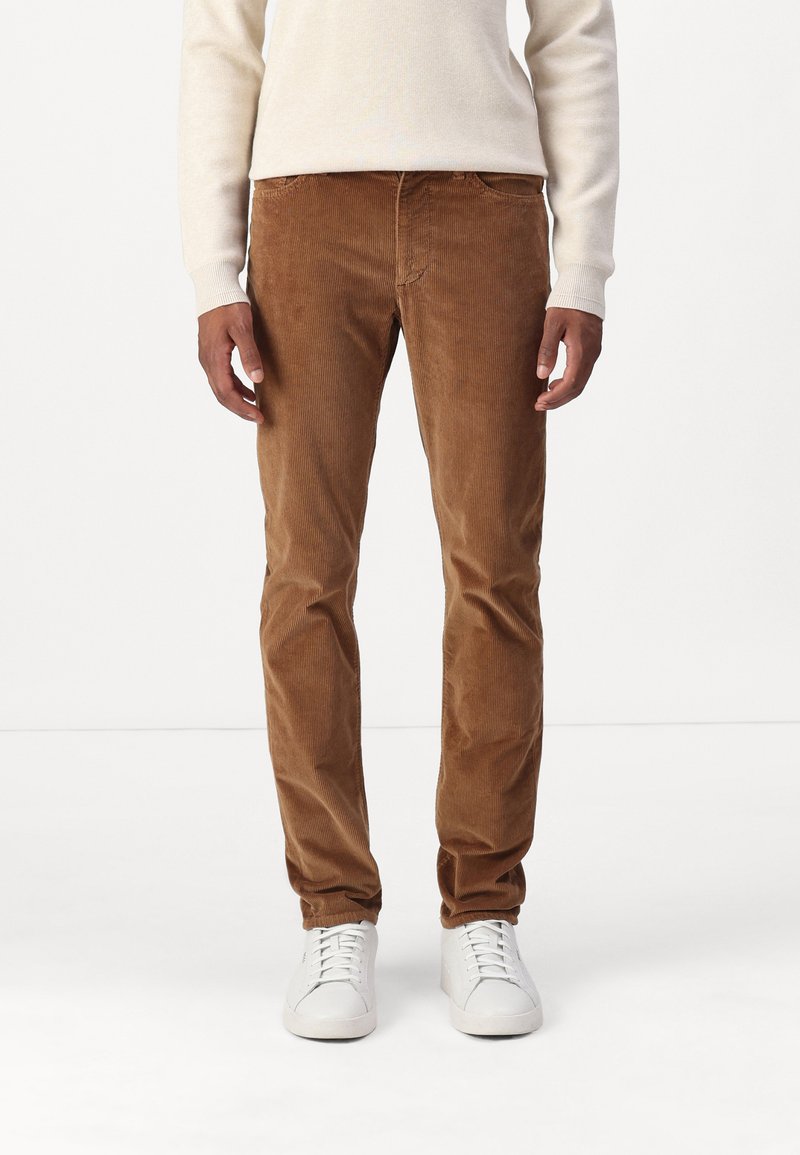 Pantalons en velours côtelé marron avec une coupe droite, présentant des côtes verticales, des poches avant, et assortis à des baskets blanches.