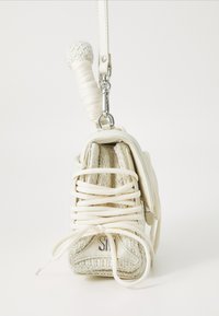 Hvid håndtaske, der ligner en sneakers, med tekstureret stof og læder, snørebånd og et dekorativt sportsinspireret håndtag. Sølvfarvet hardwaredetalje.