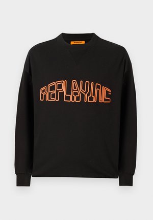 Svart hettegenser laget av bomull med v-hals og lange ermer. "REPLAYING" er trykket i oransje, omkranset i en rund stil.