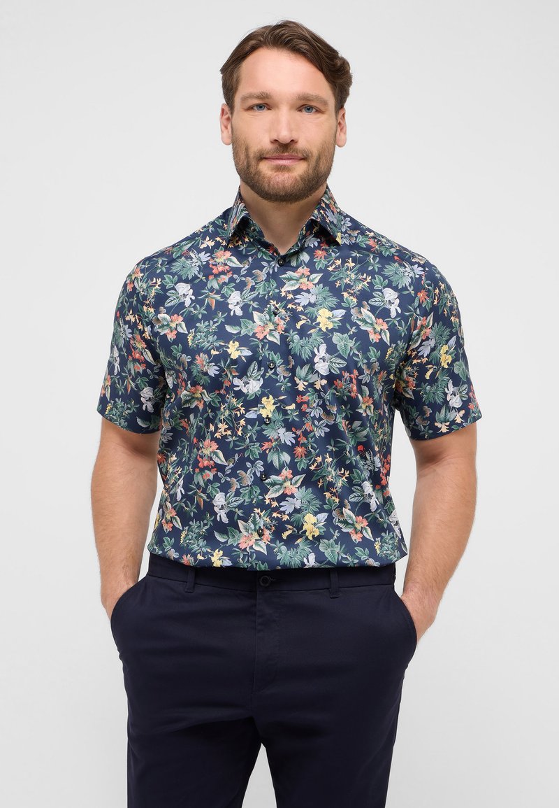 Korte mouwen overhemd in donker marineblauw stof met een kleurrijk bloemenpatroon. Heeft een traditionele kraag en een knoopsluiting aan de voorkant.
