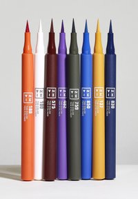 Åtta färgade eyeliners arrangerade i rad. Färgerna inkluderar orange, vit, mörkröd, lila, mörkgrön, blå, gul och marinblå, med spetsiga tips.