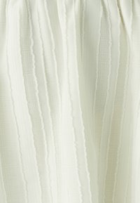 Gestructureerde stof in zacht wit, met afwisselende verticale strepen en lichte variaties in de weving, wat een subtiel en elegant ontwerp creëert.