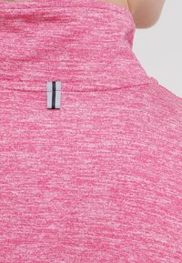 Nahaufnahme eines rosa bedruckten Stoffkragens mit einer kleinen reflektierenden Schlaufe, die in der Mitte auf der Rückseite angenäht ist.