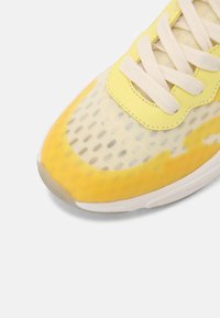 Avant d'une basket jaune et blanche avec dessus en mesh, lacets blancs et semelle en caoutchouc sur fond blanc.