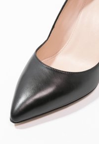 Gros plan sur une chaussure à talon haut noire en cuir à bout pointu, avec une texture lisse et une doublure intérieure beige.
