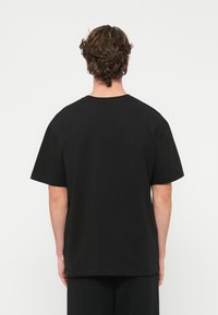 Čierne bavlnené tričko, voľný strih, zaoblený výstrih, krátke rukávy, bez viditeľných log, hladká textura, detail so zárezom na boku pri spodnom okraji.