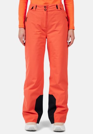 Helle orange Skihosen mit glatter Textur, ausgestattet mit schwarzen Akzenten an den Unterschenkeln, zwei Reißverschlusstaschen vorne und einem Knopfverschluss.