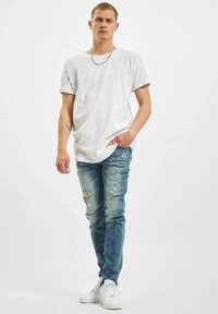 Hvit bomulls t-skjorte med rullede ermer, parret med falmede blå denimjeans med rifter. Brukt med hvite sneakers og en sølvkjede.