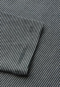 Tessuto di cotone con strisce sottili bianche e blu scuro alternate, con una vista ravvicinata di un bordo piegato che mostra una texture liscia.