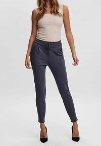 Grå tapered jogger-byxor med elastisk midja, snörning och sidofickor. Slät tyg i kombination med svarta högklackade skor.