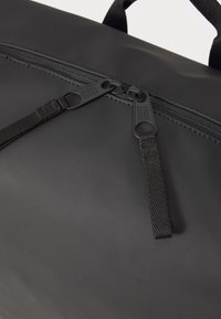 Svart duffelbag med en jevn, matt overflate. To svarte glidelåsknapper og teksturerte stoffstropper er synlige, noe som sikrer trygg lukking.