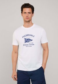 Camiseta de algodón blanca de manga corta; presenta texto e ilustraciones impresas en azul, incluyendo "Edición Costera" y un diseño de bandera.