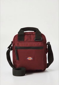 Mala de tecido bordeaux com alça de mão superior, alça ajustável, bolso frontal com fecho éclair e emblema do logótipo Dickies. Design robusto e compacto.