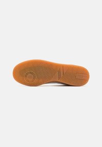 Suela de goma con patrón texturizado, que presenta un logo circular y el nombre de la marca. Color naranja vibrante con una superficie lisa y duradera.