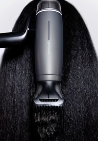 Cheveux noirs étant lissés avec une brosse lissante ghd speed noire et grise sur fond blanc.