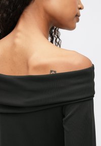 Μαύρη μπλούζα χωρίς ώμους με μαλακό ύφασμα και λεία υφή, που διαθέτει πτυχωτό λαιμό και διακριτική ρυθμισμένη λεπτομέρεια.