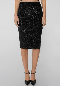 Jupe crayon noire avec des embellissements en sequins texturés, longueur genou et silhouette cintrée. Assortie à des escarpins noirs à bout pointu.