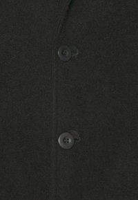 Tissu en mélange de laine noir avec une texture lisse et deux boutons foncés à l'avant, dans un design classique de chemise.