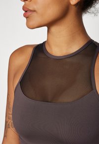 Top desportivo em mauve escuro com um painel de malha preta translúcida na gola, apresentando uma textura canelada e um tecido sólido contrastante.