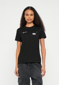 Čierne bavlnené tričko s okrúhlym v�ýstrihom, krátkymi rukávmi a výraznou grafikou so štýlizovanou tvárou a diagonálnymi pruhmi.