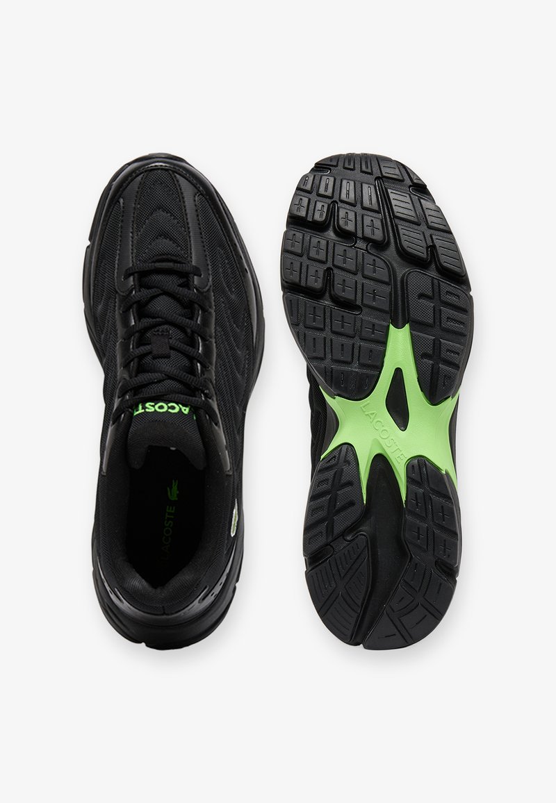 Chaussures de sport noires avec tige en mesh ; une chaussure montre une vue de dessus avec des lacets noirs, l'autre montre la semelle avec un accent vert et une bande de roulement texturée.