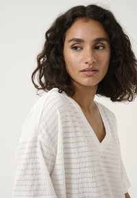 White textured V-neck top with loose-fitting sleeves, featuring a subtle striped pattern. Light fabric with a relaxed, breathable feel.