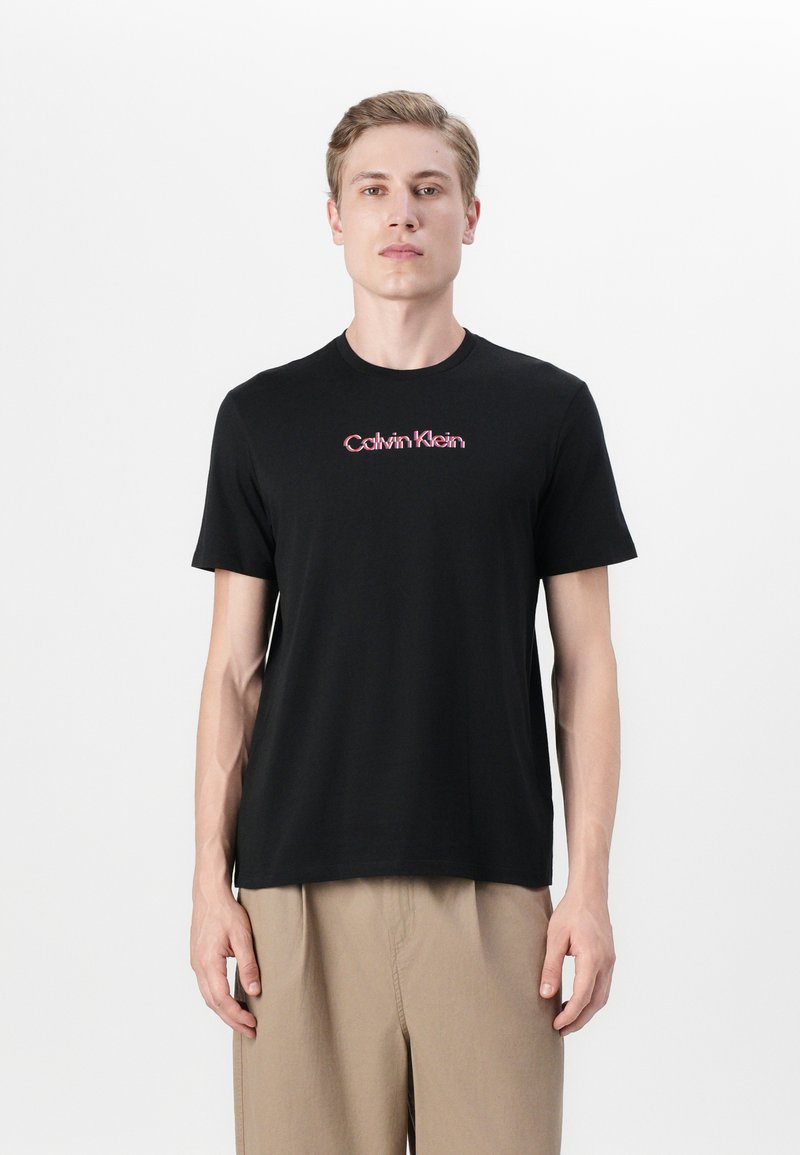 Black cotton T-shirt with short sleeves and round neckline, featuring a red Calvin Klein logo across the chest. Smooth texture, relaxed fit.