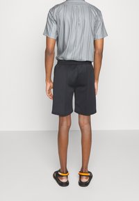 Camisa de manga corta con cuello en gris con rayas verticales; combinada con pantalones cortos negros y sandalias negras con detalles en naranja.