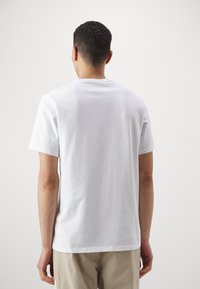 Camiseta blanca de manga corta hecha de algodón, con cuello redondo y un corte casual, que presenta una textura suave y detalles visuales mínimos.