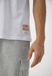 Biała bawełniana koszulka z etykietą "Hardwood Classics", zestawiona z szarymi spodniami dresowymi z boczną kieszenią i dyskretnym haftem logo.