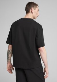 Černé tričko s krátkým rukávem z bavlny s volným střihem, s kulatým výstřihem a hladkým povrchem. Jednoduchý design, bez viditelných log.