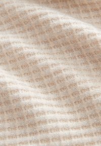 Beige strukturierter Stoff mit einem Rautenmuster und subtilen metallischen Fäden, der ein sanftes und leicht schimmerndes Aussehen erzeugt.
