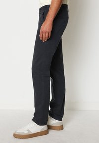 Pantaloni dritti blu navale realizzati in tessuto misto cotone, con un dettaglio a bottone sulla tasca posteriore. Abbinati a sneakers bianche.