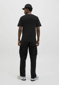 Sort bomulds T-shirt med rund hals, parret med sorte cargo bukser med lommer, iført grå og sorte træningssko.