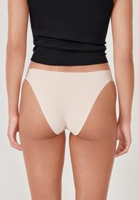 Bikini briefs beige a vita bassa realizzati in tessuto liscio, con copertura minimale e un design senza cuciture con dettagli in pizzo ai lati.
